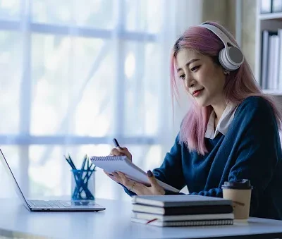 asian female college student wearing headphones studying online with laptop computer surfing